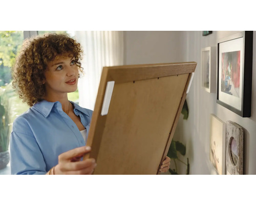 Vrouw bevestigt fotolijst met plakstrips aan de muur