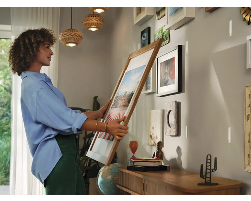 Vrouw hangt een fotolijst op aan een muur met meerdere lijsten.