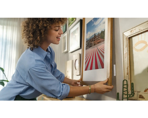 Vrouw hangt een ingelijste afbeelding aan een muur