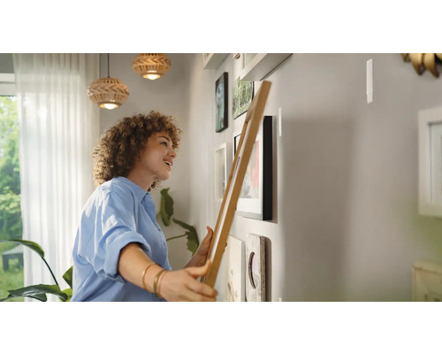 Vrouw hangt fotolijsten aan een muur