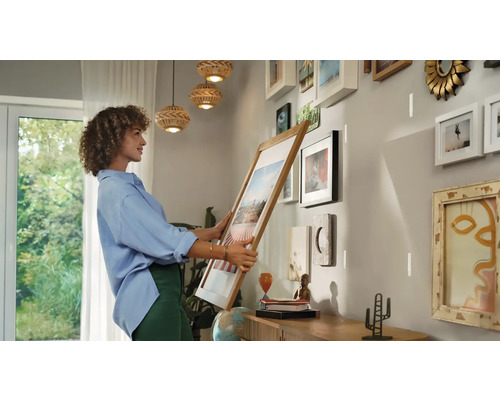 Vrouw hangt fotolijst aan de muur in een lichte kamer