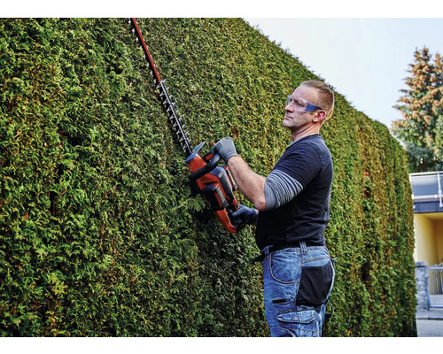 Een man snoeit een heg met een heggenschaar en draagt een veiligheidsbril.