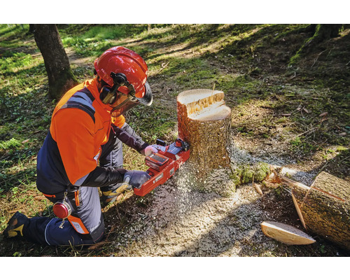 Een persoon met beschermende kleding gebruikt een kettingzaag op een boomstronk.