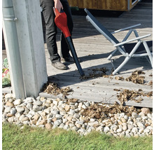 Een persoon maakt met een bladblazer een houten terras schoon van bladeren