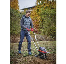 Een man gebruikt een tuinfrees in de tuin om de grond te bewerken.