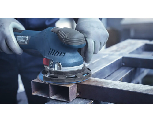 Een man schuurt een metalen werkstuk met een excentrische schuurmachine.