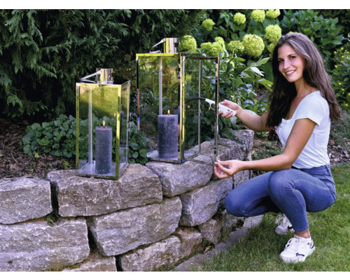 Vrouw steekt kaars aan in windlicht in de tuin