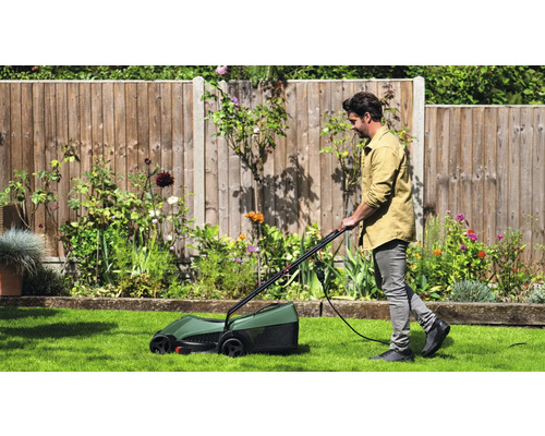 Een man maait het gazon met een elektrische gazonmaaier in een tuin.