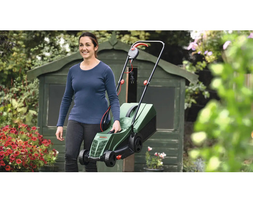 Vrouw draagt een elektrische grasmaaier in de tuin voor een tuinhuis.