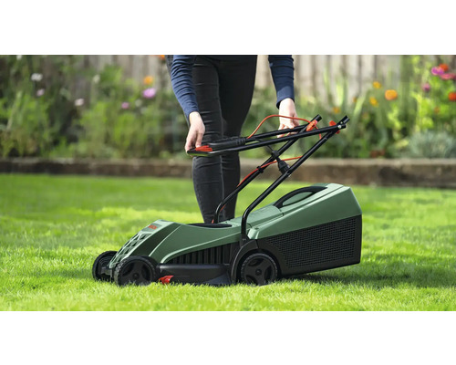 Een persoon bedient een groene grasmaaier op een gazon.