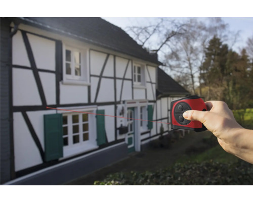 Hand gebruikt een laser afstandsmeter op een vakwerkhuis