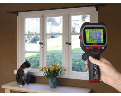 Een hand houdt een warmtebeeldcamera voor een raam, terwijl een kat op de vensterbank zit.