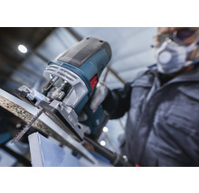 Een decoupeerzaag snijdt een werkstuk, bediend door iemand met beschermende kleding.