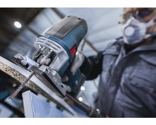 Een decoupeerzaag snijdt een werkstuk, bediend door iemand met beschermende kleding.