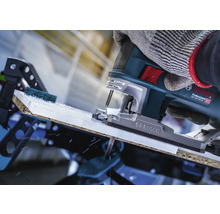 Close-up van een decoupeerzaag die een werkstuk snijdt, bediend door een persoon met handschoenen.