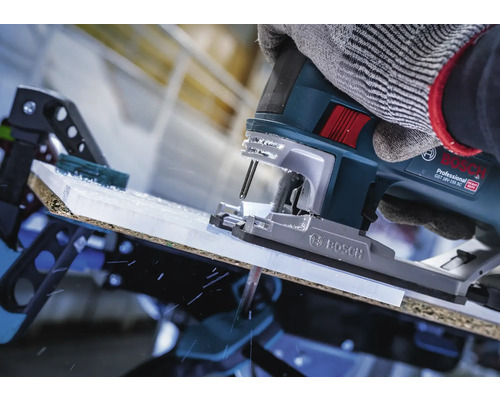 Close-up van een decoupeerzaag die een werkstuk snijdt, bediend door een persoon met handschoenen.