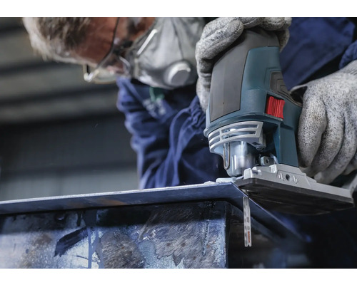 Een persoon met een ademhalingsmasker zaagt een stuk metaal met een decoupeerzaag.