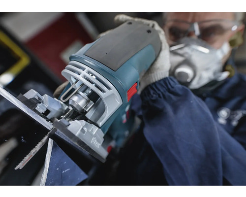 Een decoupeerzaag in gebruik bij het zagen van materiaal, bediend door een persoon met een veiligheidsmasker en een veiligheidsbril.