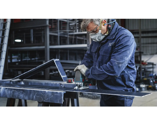 Een vakman snijdt een stuk metaal met een decoupeerzaag. Hij draagt beschermende kleding.