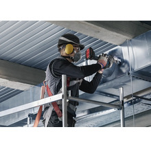 Een man staat op een steiger en bewerkt een metalen buis met een pijpenbuiger.