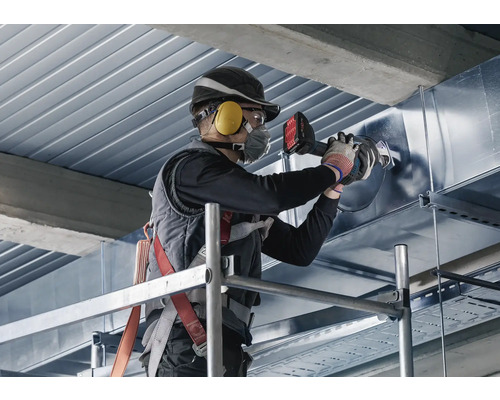 Een man staat op een steiger en bewerkt een metalen buis met een pijpenbuiger.