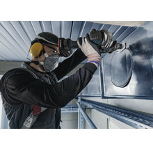 Een persoon gebruikt een knabbelschaar om een gat in een ventilatiekanaal te knippen.