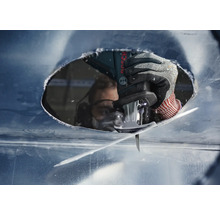 Close-up van een persoon met veiligheidsbril die met een decoupeerzaag een gat in een metalen plaat zaagt.