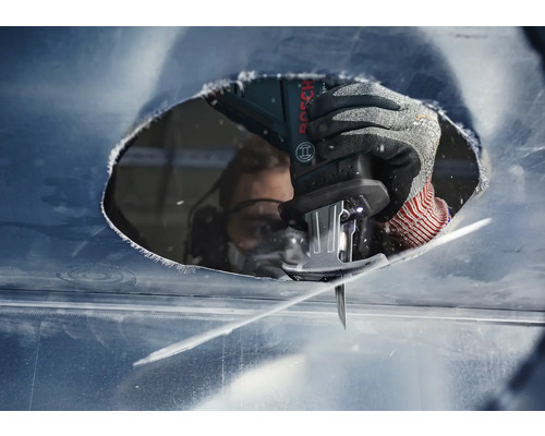 Close-up van een persoon met veiligheidsbril die met een decoupeerzaag een gat in een metalen plaat zaagt.