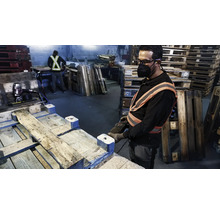 Arbeider repareert houten pallets met gereedschap in een werkplaats.