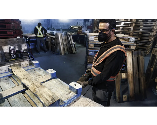 Arbeider repareert houten pallets met gereedschap in een werkplaats.