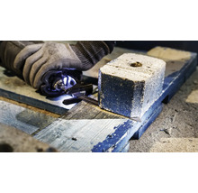 Een persoon zaagt een houtskoolbriket op een houten plank met een zaag.