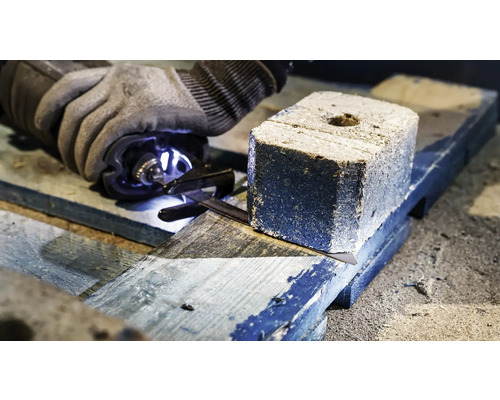 Een persoon zaagt een houtskoolbriket op een houten plank met een zaag.