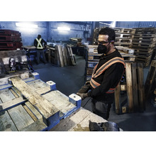 Een arbeider repareert een pallet met een pneumatische tacker in een fabriekshal.