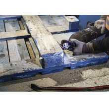 Iemand zaagt een houten pallet met een reciprozaag. Een koevoet ligt op de grond.