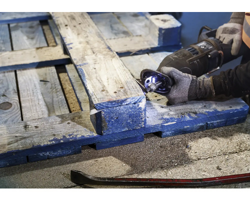 Iemand zaagt een houten pallet met een reciprozaag. Een koevoet ligt op de grond.