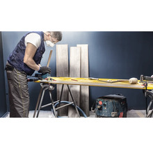 Vakman snijdt laminaat met een decoupeerzaag op een werkbank. Op de achtergrond staan laminaatplanken.