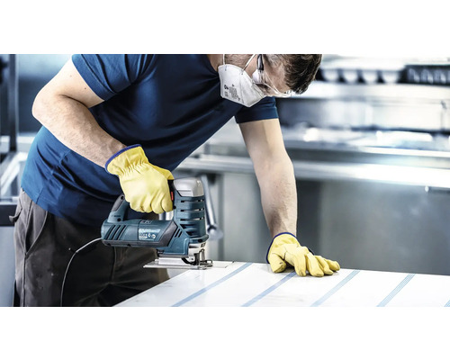 Ambachtsman met veiligheidsmasker, veiligheidsbril en handschoenen zaagt een werkstuk met een decoupeerzaag.