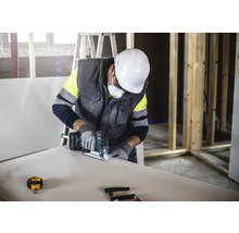 Een vakman zaagt een gipsplaat met een decoupeerzaag terwijl hij beschermende kleding draagt.