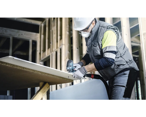 Een bouwvakker snijdt een gipsplaat met een decoupeerzaag op een bouwplaats