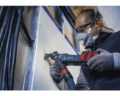 Ambachtsman zaagt met een multifunctioneel gereedschap een gat in een gipsplatenwand