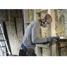 Vakman met ademhalingsmasker en veiligheidsbril die met een multifunctioneel gereedschap in een casco werkt