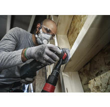 Ambachtsman bewerkt hout met een multifunctioneel gereedschap, inclusief stofafzuiging, veiligheidsbril en adembescherming.