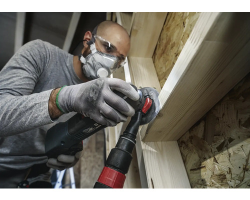 Ambachtsman bewerkt hout met een multifunctioneel gereedschap, inclusief stofafzuiging, veiligheidsbril en adembescherming.