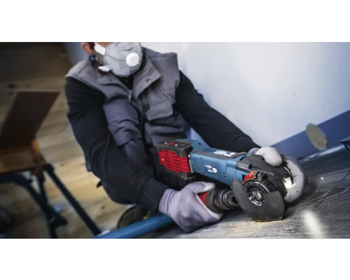 Ambachtsman gebruikt een haakse slijper met stofafzuiging op een houten vloer