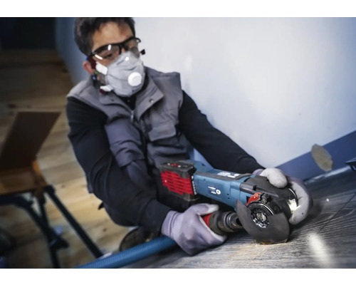 Man werkt met een haakse slijper op een vloerbedekking, persoonlijke beschermingsmiddelen zijn aanwezig