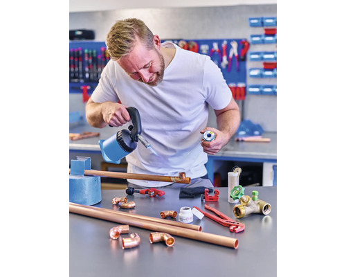 Man soldeert koperen buizen met een soldeerbout en soldeertin in een werkplaats.