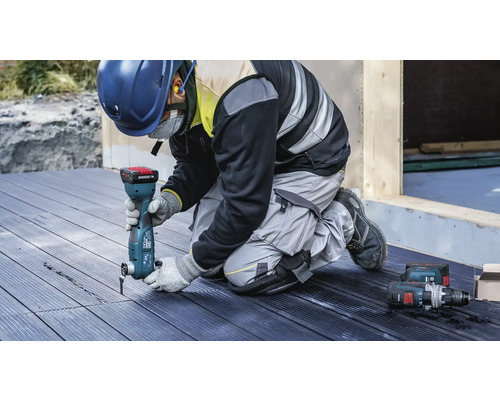 Een vakman gebruikt een multifunctioneel gereedschap op een houten terras. Ook is er persoonlijke beschermingsmiddelen aanwezig.