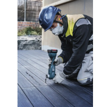 Een bouwvakker met veiligheidshelm en gezichtsmasker gebruikt een multifunctioneel gereedschap om een groef in een terrasplank te snijden.