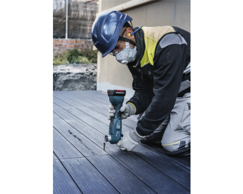 Een bouwvakker met veiligheidshelm en gezichtsmasker gebruikt een multifunctioneel gereedschap om een groef in een terrasplank te snijden.