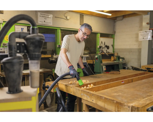 Een man maakt een werkbank schoon met een stofzuiger in een werkplaats.